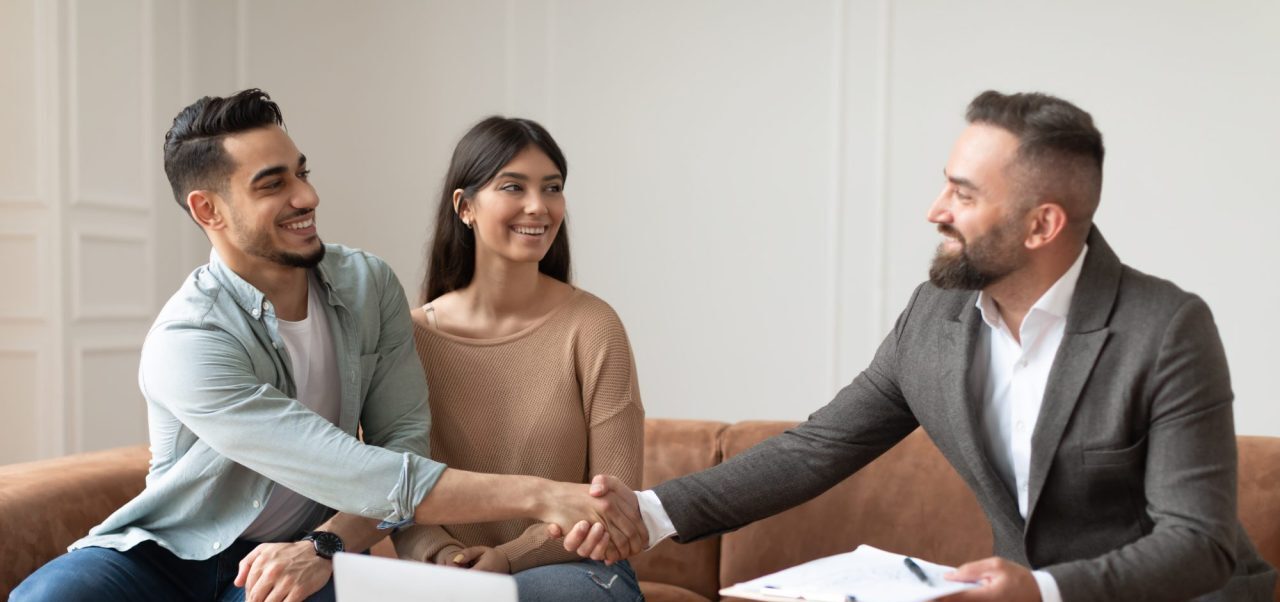 millennial-couple-buying-new-apartment-shaking-hands-with-realtor-e1695129370216